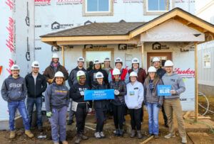 A group of 16 volunteers standing in front of a home that does not have siding on it yet.