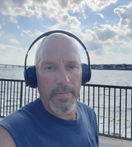 Scott Cabral taking selfie in front of water with a railing behind him.