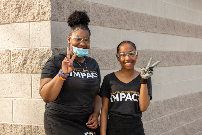 Two female Benton Harbor students pose on Community Day of Impact with smiles and peace signs