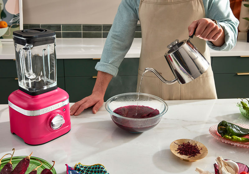 KitchenAid blender in Hibiscus color, with person pouring hot water on a purple-pink mixer in a bowl