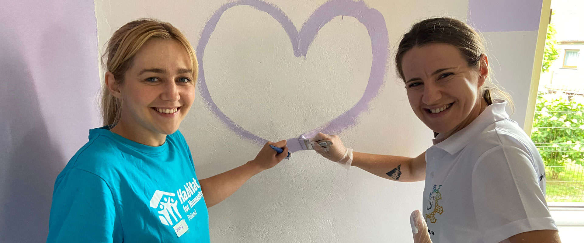 Two Whirlpool employees in Poland paint a purple heart on the wall at a Habitat for Humanity build
